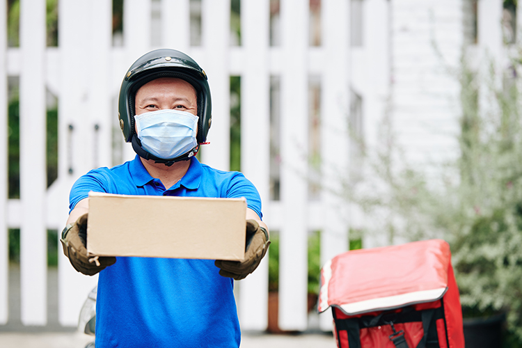 Smiling Asian delivery man in medical mask giving cardboard box